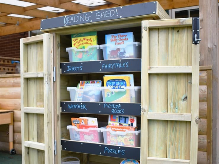 A well-organised Acorn Store being used as a Reading Shed with plastic containers on each shelf containing books.