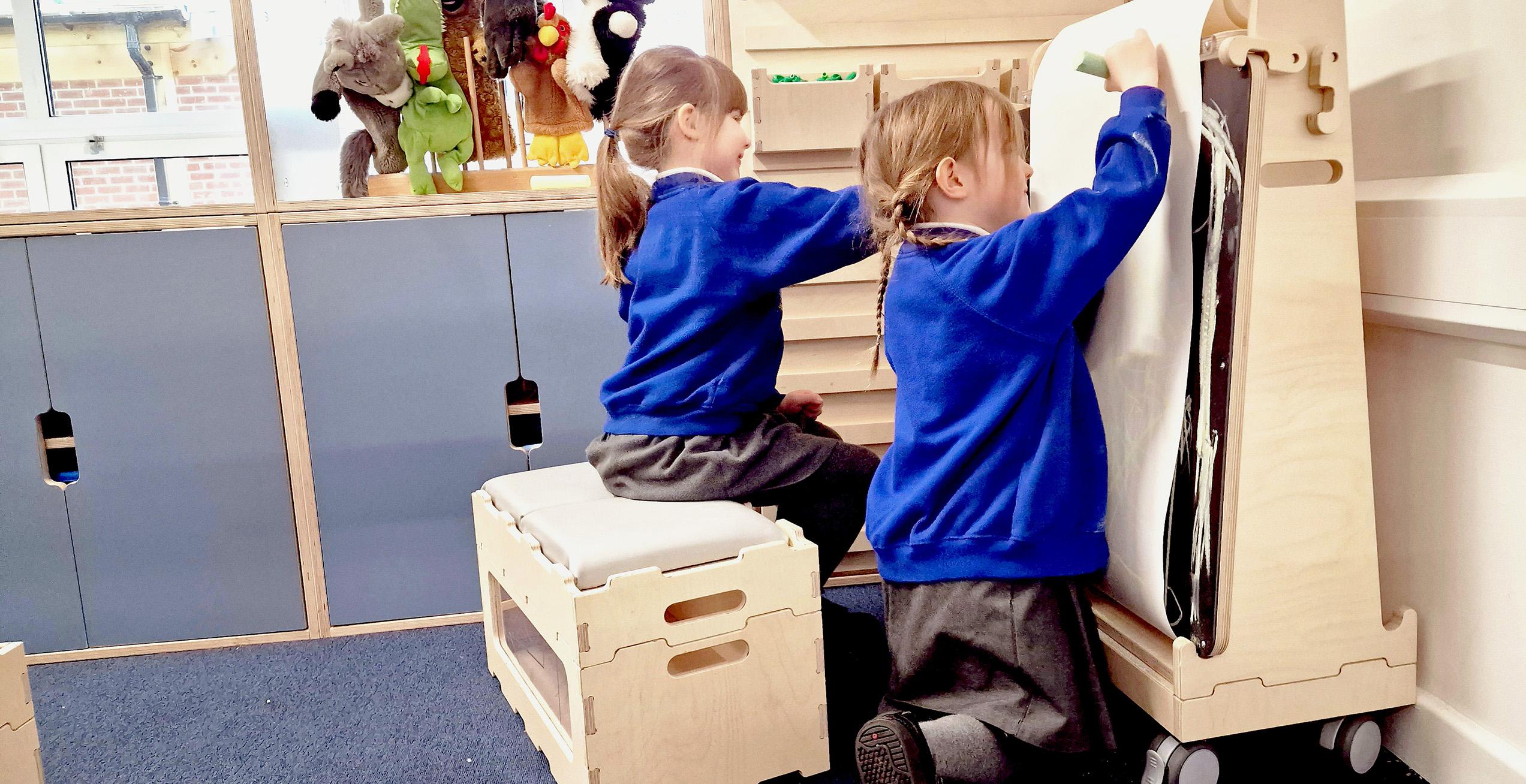 two primary school students drawing on art easel sat on Stack And Sit stools