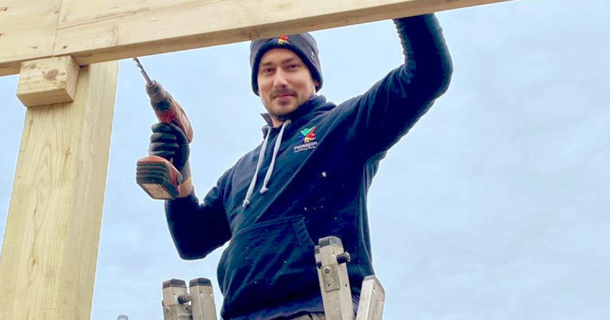 builder smiling at the camera with a drill in hand, installing a playground