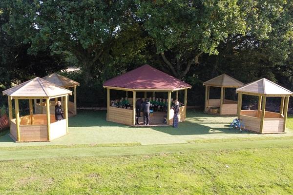 Outdoor classroom area at Ewloe Green Primary, featuring five wooden gazebos with a larger central gazebo, providing shaded spaces for outdoor lessons and activities.