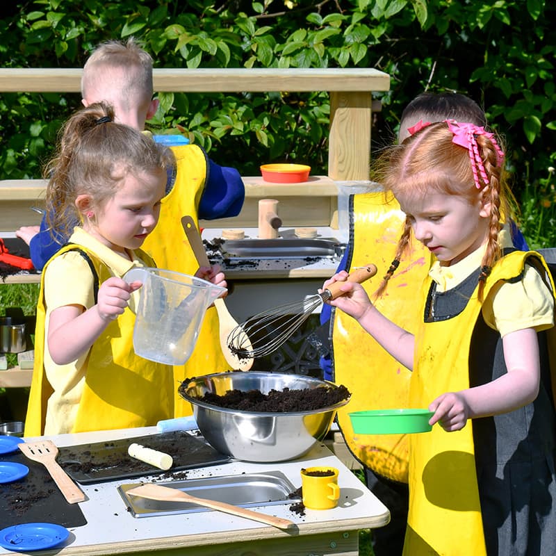 reception aged children playing with mud kitchen in nursery school playground