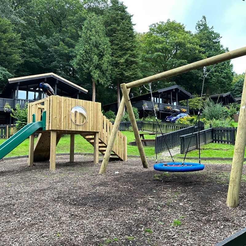 wooden play tower and large swing on wood chip surface in holidy park playground