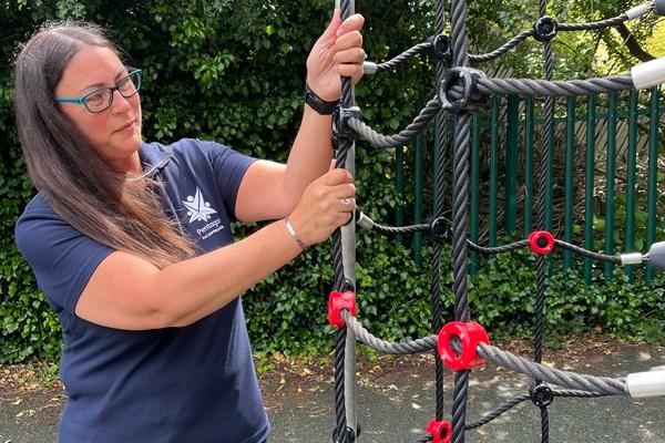 A playground inspector is giving a rope climbing net a pull to ensure that the rope is properly attached to the playground equipment