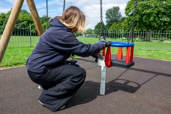 A playground inspector is checking the height of a swing set from the ground to the seat