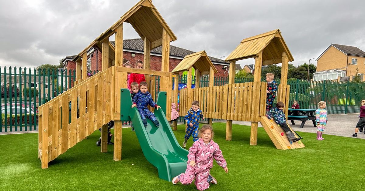 A group of EYFS children are playing on a Goodrich Modular Play Tower and are having fun after a playground inspection