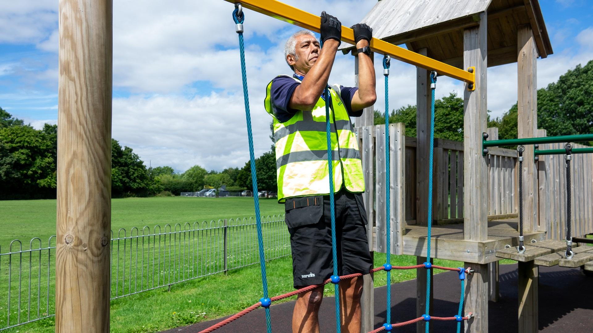 A man is testing the strength of a metallic bar that is attached to a rope climbing frame. The main is putting his body weight on the rope climbing frame