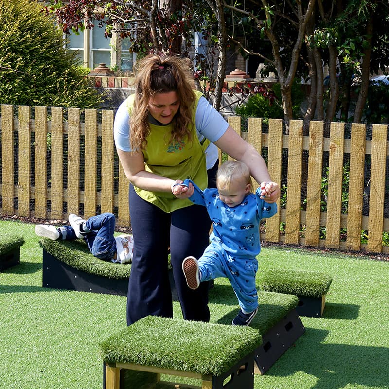 teacher helping a nursery child jump from one Get Set, Go! Block to another in outdoor play area