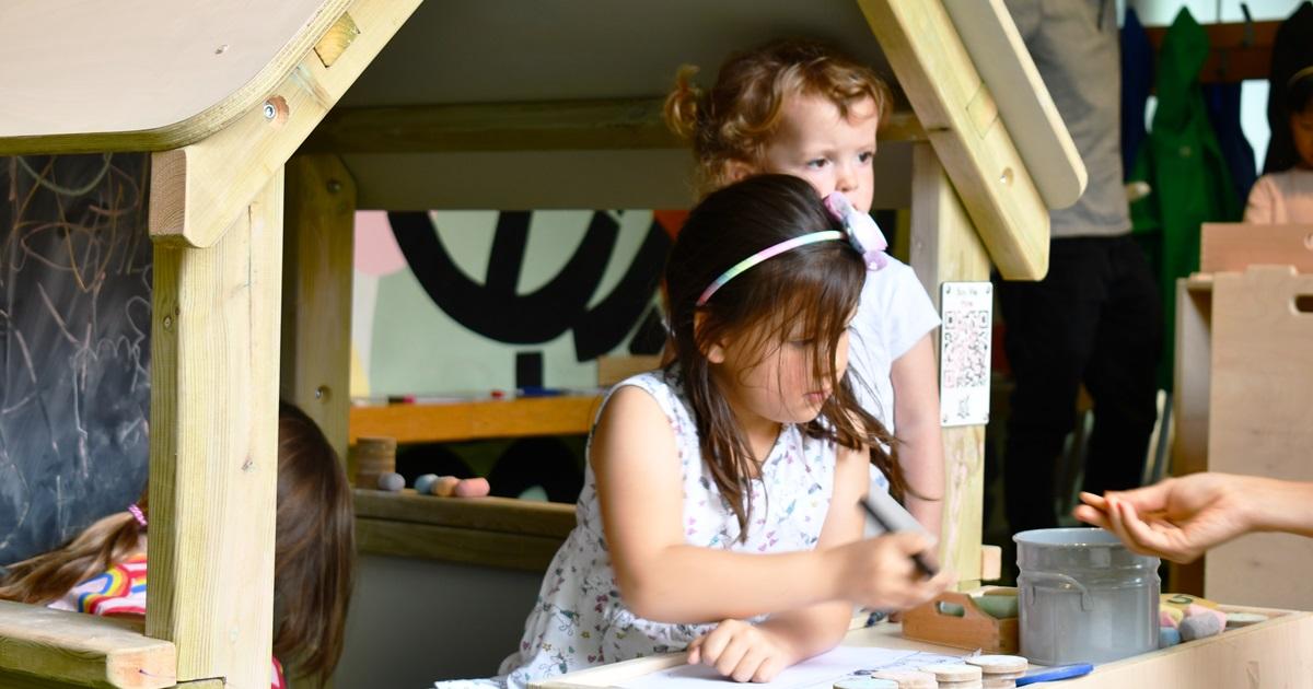 two young children playing in a wooden playhouse outside