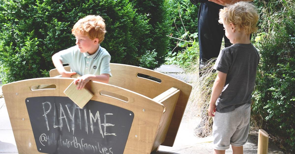 child stood in large wooden play skip getting a building block to play with