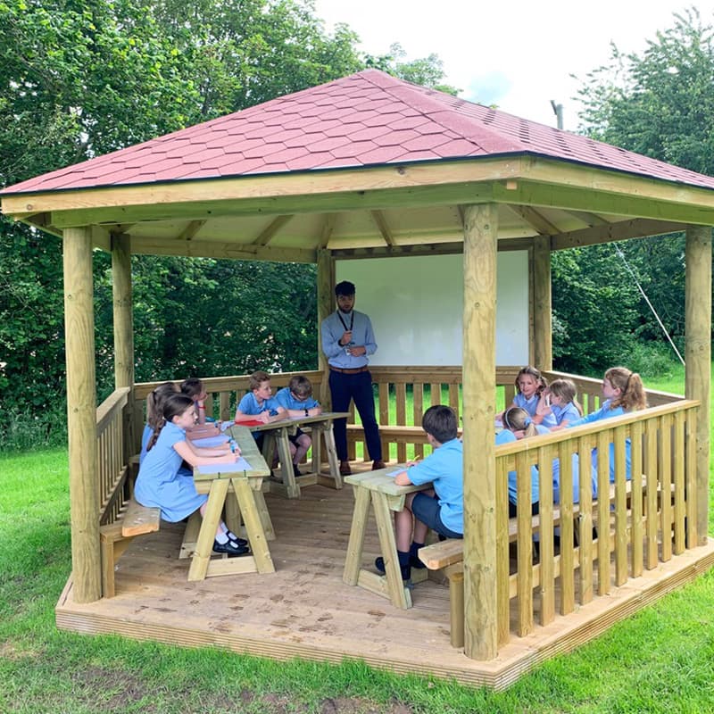 a teacher with a small class of 12 primary aged students having an outdoor lesson in a gazebo outdoor classroom