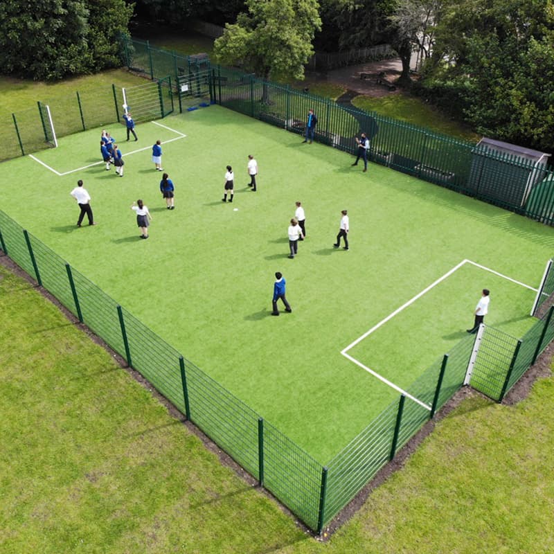 key stage 2 children playing football in multi use games area outside