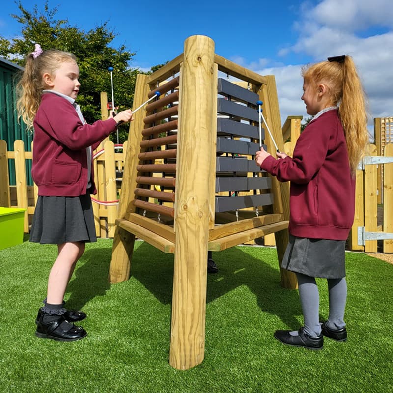 two primary school pupils making music with the Pentagon Play Music Triad outside in school playground area on astroturf