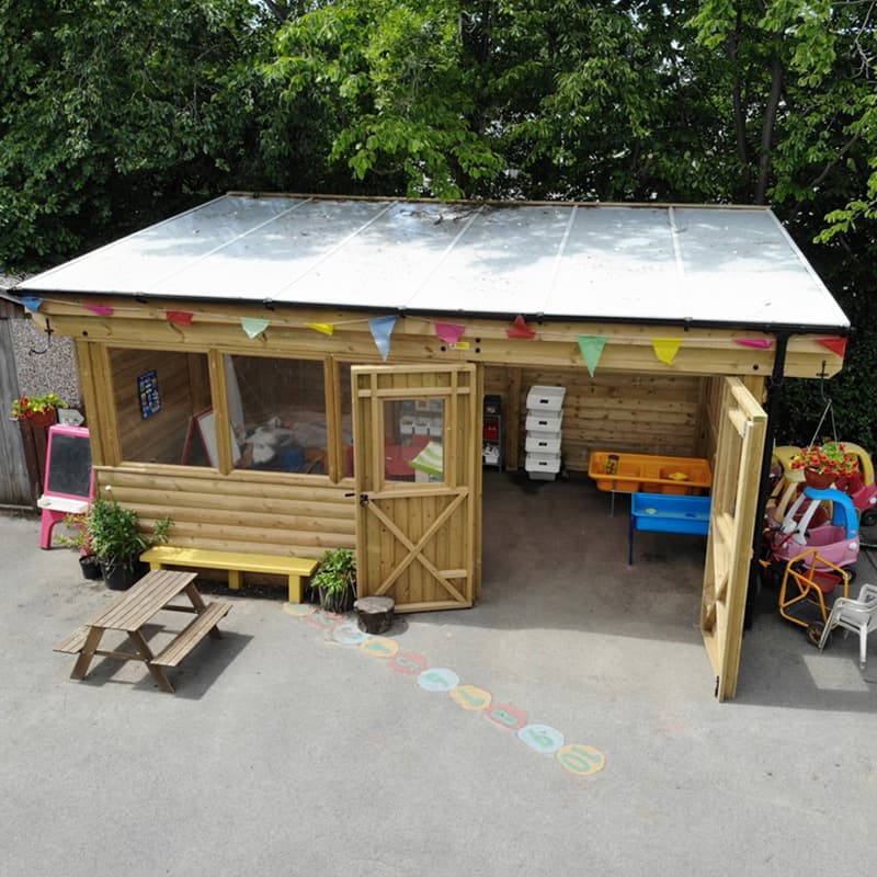 wooden outdoor classroom with storage, water tables, easels, and bunting around the roof