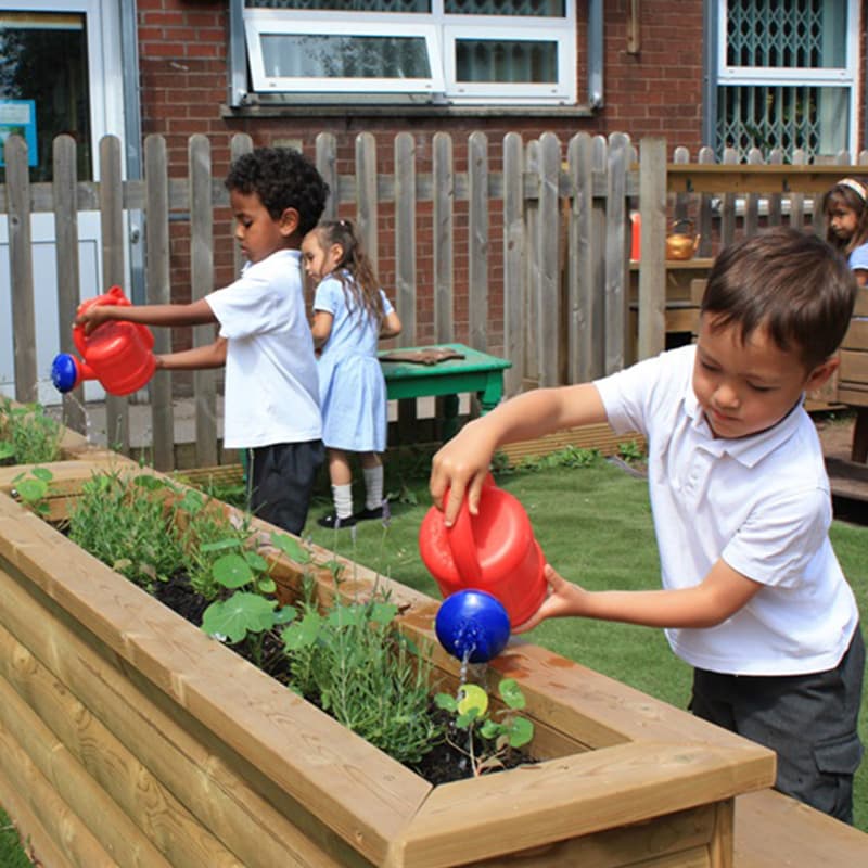 primary school children watering flowers in their school planters outside in the playground