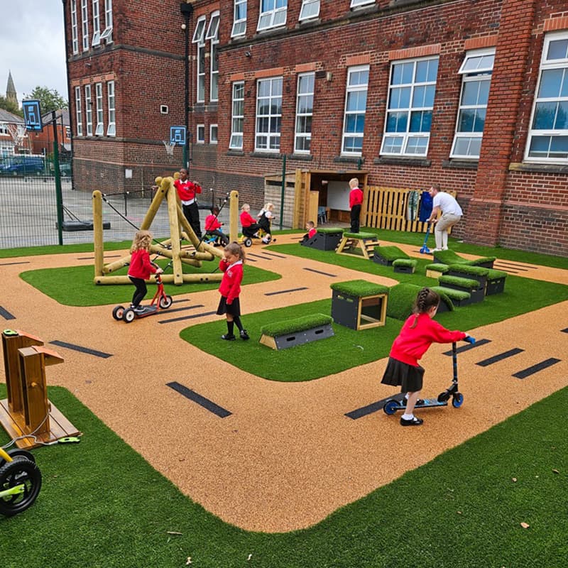 key stage 1 primary school children riding scooters on tracks in outdoor playground