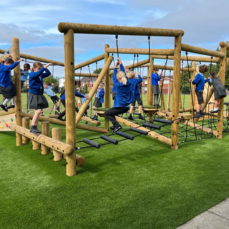 primary school children playing on a trim trail climbing frame in a playground on the grass