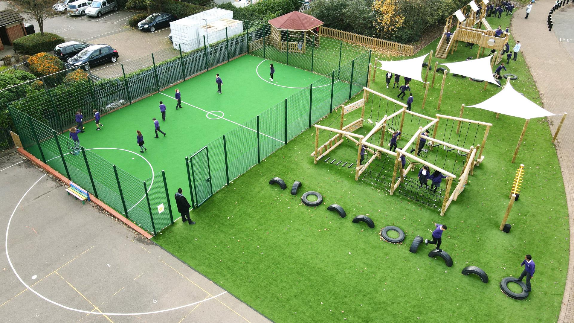 multi-use-games-area with artificial grass and fencing alongside a clmbing frame, play tower, outdoor classroom and tyre trim trail
