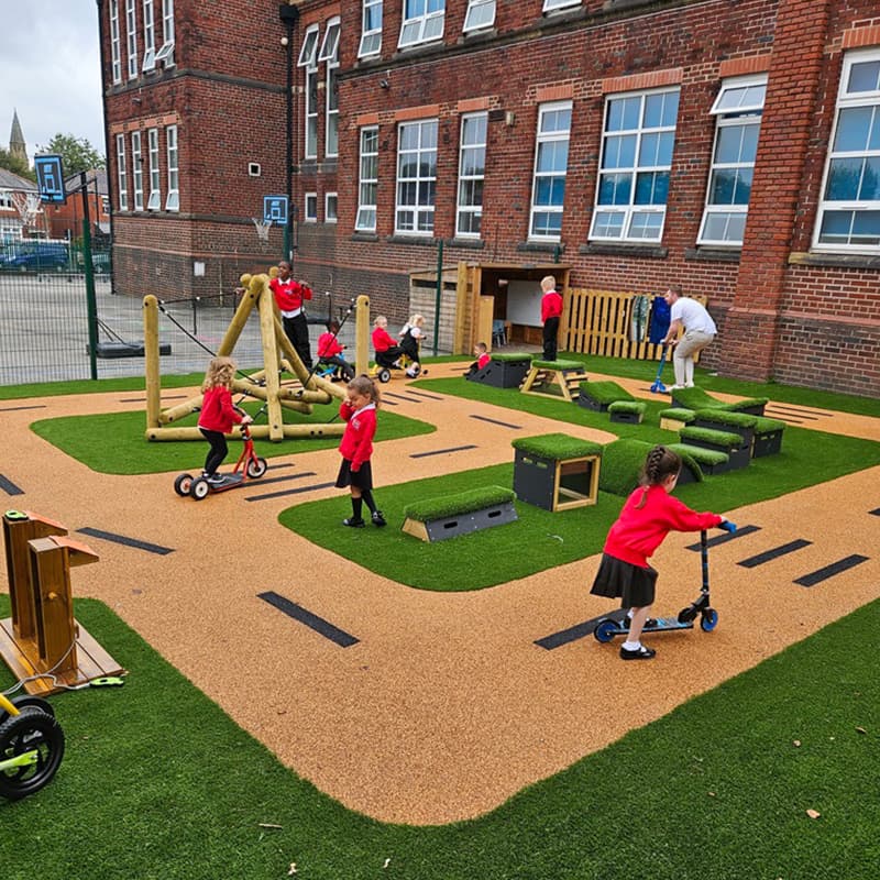 key stage 1 primary school children riding scooters on tracks in outdoor playground
