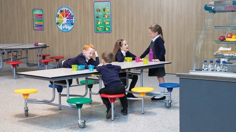primary school children sitting and talking around a SpaceRight school dining table in a canteen